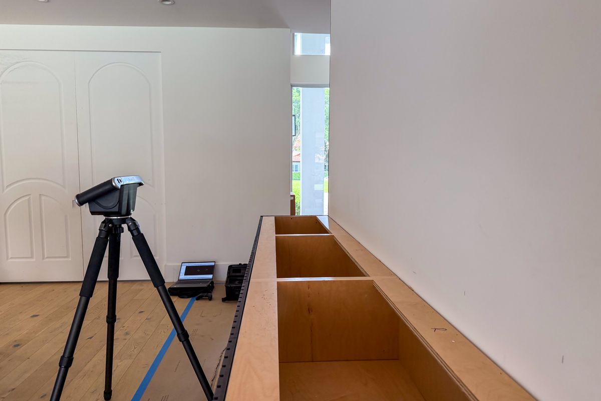 A Flexijet laser measuring head mounted on a tripod beside an installed cabinet run, set up to template the countertop before the stone is cut.